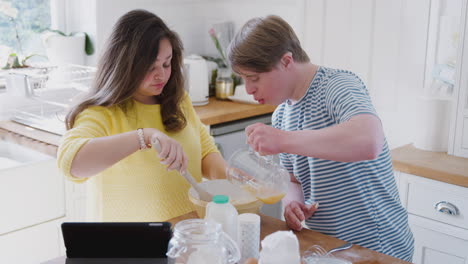 Junges-Down-Syndrom-Paar-Befolgt-Rezept-Auf-Digitalem-Tablet,-Um-Zu-Hause-In-Der-Küche-Kuchen-Zu-Backen