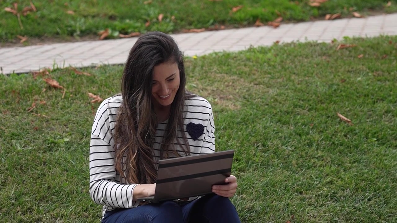 Una giovane donna che lavora con entusiasmo al suo portatile godendosi l'ambiente di un parco.