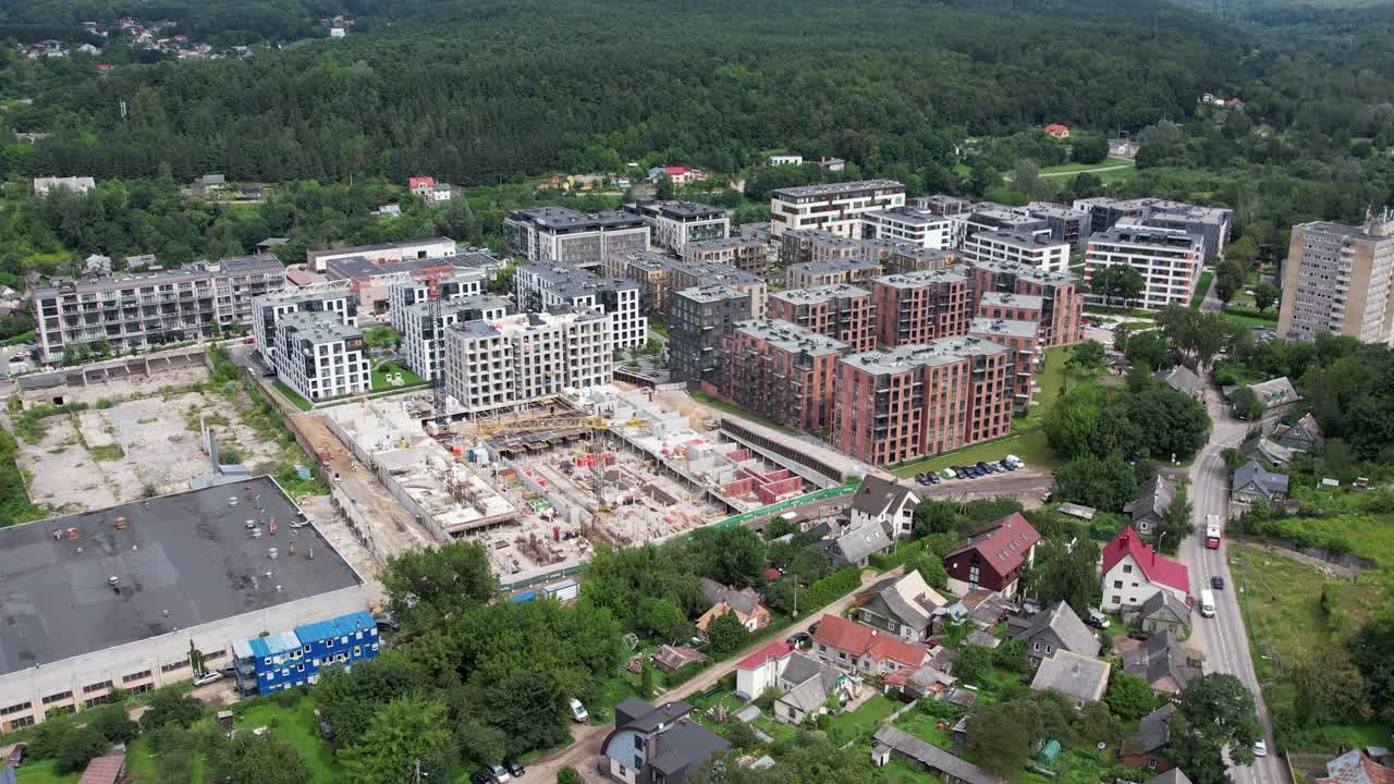 Ảnh chụp từ trên không bằng drone khu căn hộ hiện đại bên cạnh khu rừng, với công trường xây dựng đang hoạt động và những ngôi nhà ở vùng ngoại ô lân cận — sự tăng trưởng bất động sản và mở rộng đô thị