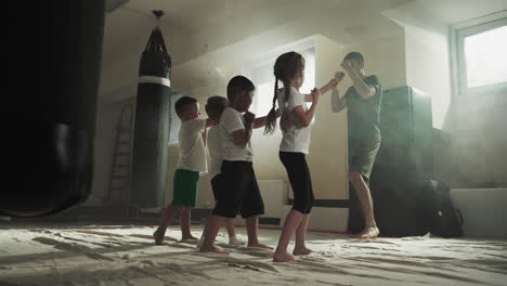 children do punches following trainer in boxing school. little sportsmen hit by hands under instructor control in gym slow motion. kids development