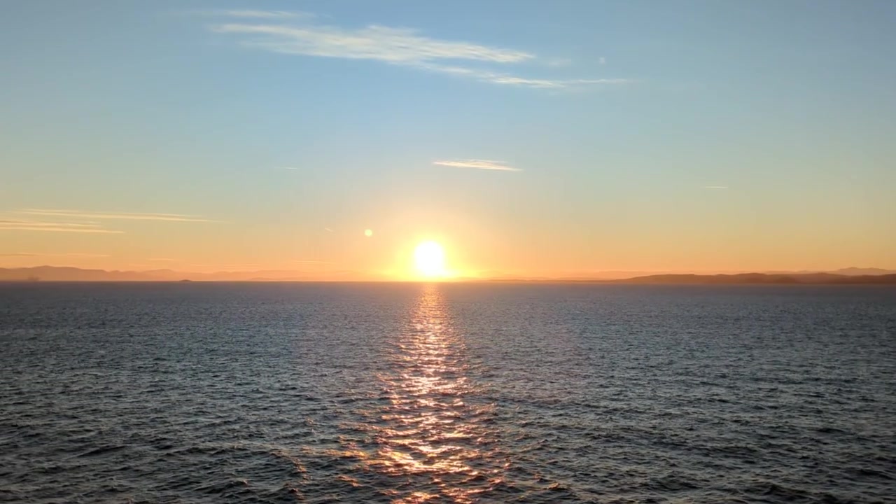 Golden Sun Setting Over Calm Ocean Horizon with Distant Land