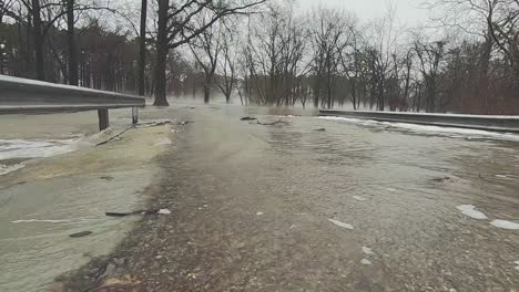 right to left pan shot of rising flood waters flowing over a road running throw a park