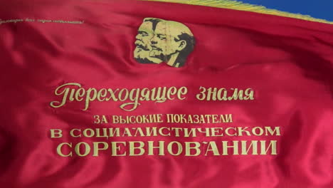 zoom out on soviet parade flag portraying karl marx and vladimir lenin flying in slow motion with vivid blue sky in background