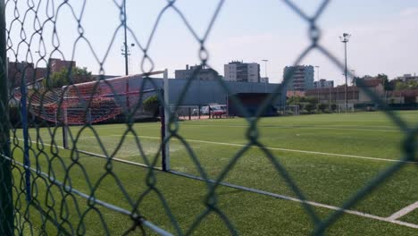 slow motion tracking wide shot of empty soccer football field through chainlink fence on hot sunny day