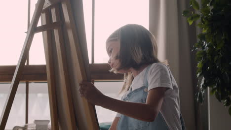 little blonde girl painting on the lectern next to the window at home