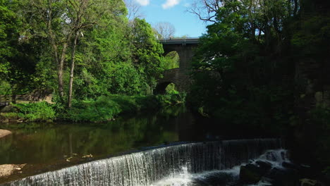 cascada pacífica en el río británico con árboles verdes y hierba exuberante bajo la pista lenta aérea del arco en el distrito de los picos