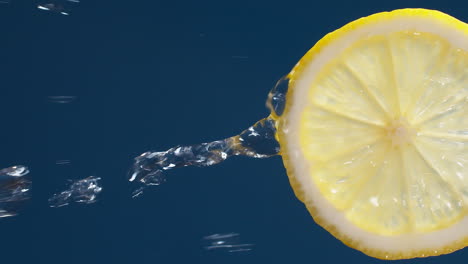 Vertikale-Zeitlupenmakroaufnahme-Von-Fließendem-Wasser-Aus-Zitronenscheibe-Auf-Blauschwarzem-Hintergrund