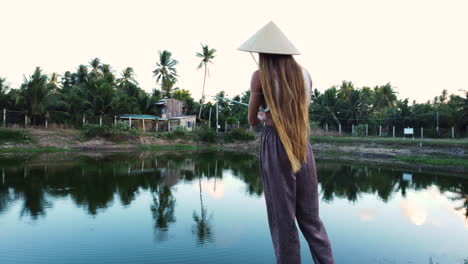 model with long blonde hair wearing asian conical hat fishing in pond in tropical paradise