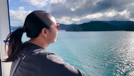 Una-Mujer-Asiática-Con-Gafas-De-Sol-Mira-Las-Aguas-Soleadas-Y-Desde-El-Ferry-En-El-Estrecho-De-Cook-En-Nueva-Zelanda,-De-Cerca