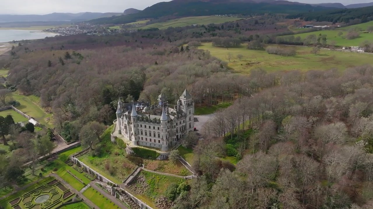 Orbita aerea di drone del Castello di Dunrobin, Sutherland, Scozia, con torrette e guglie fiabesche, giardini formali, sullo sfondo del Mare del Nord e l'iconica architettura baronale scozzese.