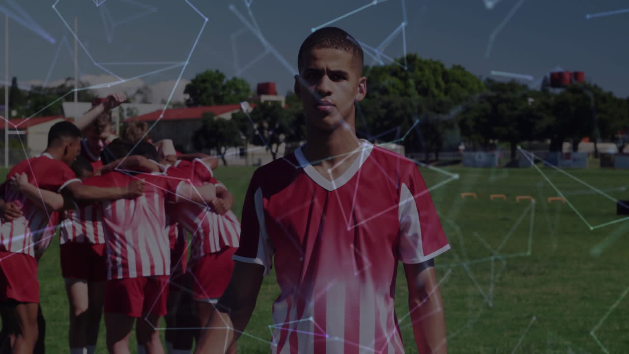 Teen soccer player standing in jersey on field, teammates huddling, network overlay tracking data