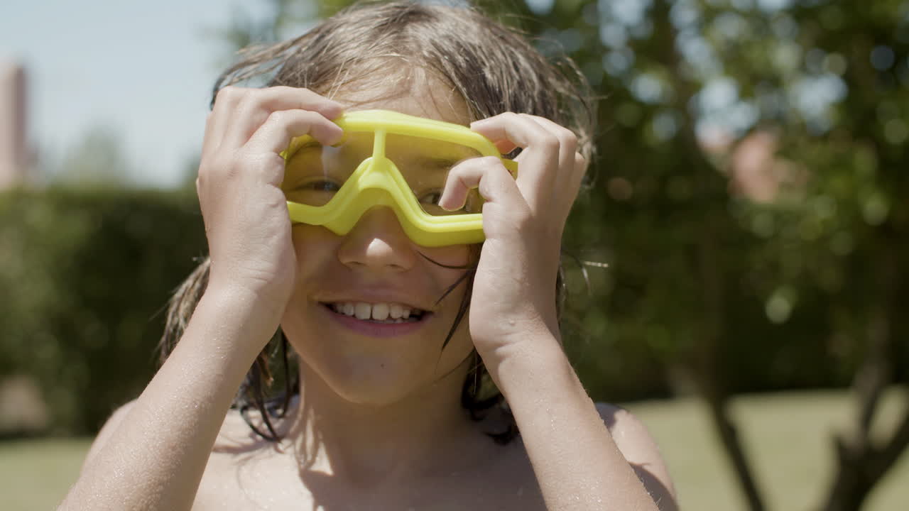 Free stock video - Front view of happy boy with naked torso and watersport goggles looking at the camera in the garden at home