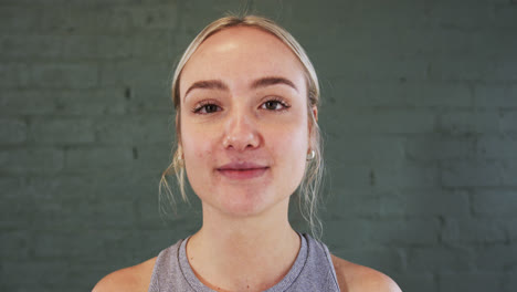 smiling caucasian young woman with blonde hair against grey brick wall in yoga studio