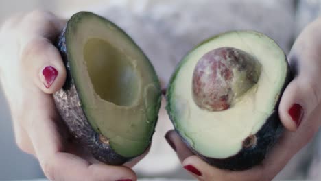 detalle de un aguacate sostenido por una niña con esmalte de uñas rojo: abre el aguacate en dos y muestra el interior con el hoyo