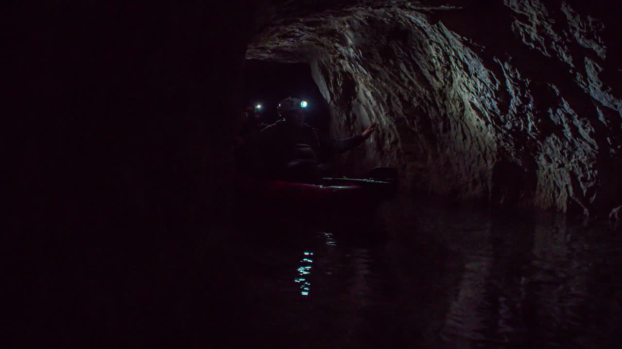 A group of people entering a dark scary cave with a flashlight on the head
