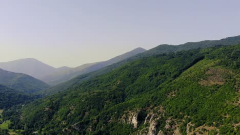 Aerial-view-over-green-old-mountains-on-bright-clear-summer-sky