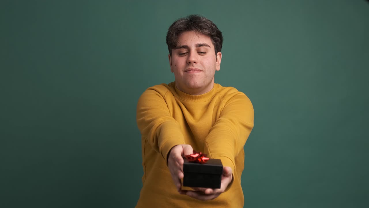 Happy man giving present box in green studio