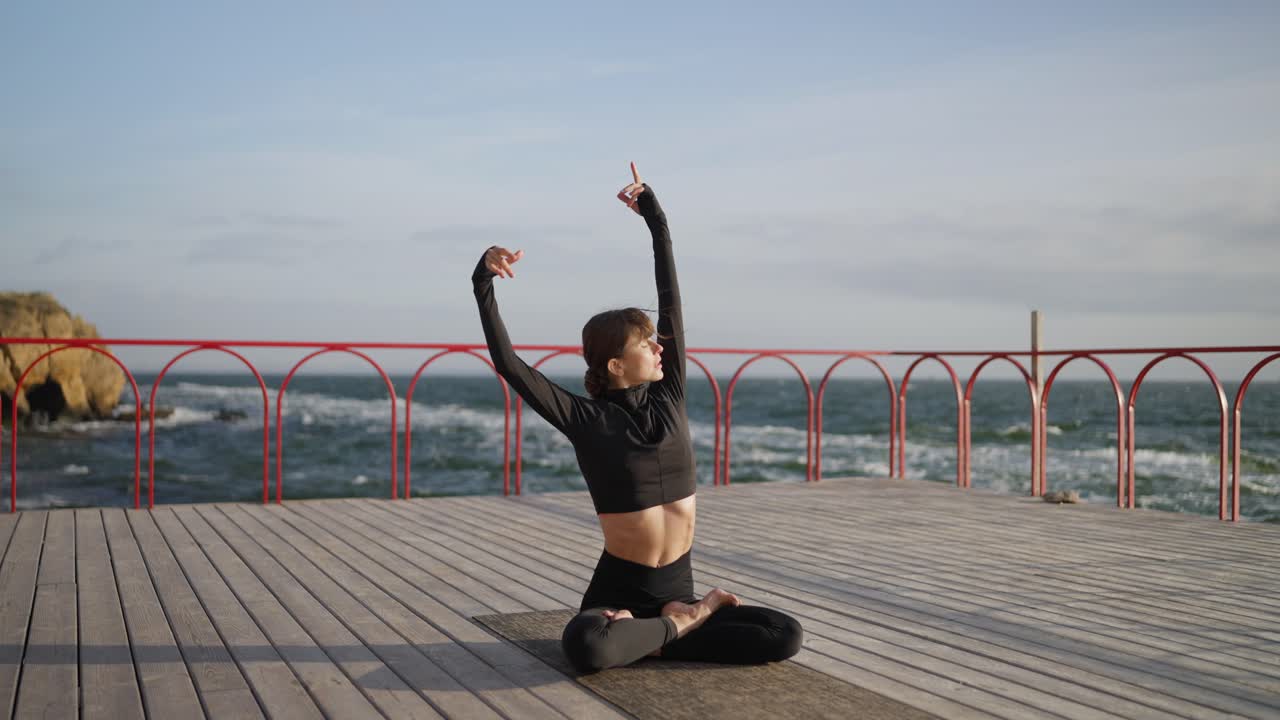 mujer practicando yoga en un muelle de madera con vistas al océano