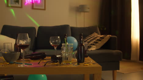 salón desordenado o sala de estar con mesa cubierta con vasos de vino vacíos y botellas de cerveza después de la fiesta de la casa 1