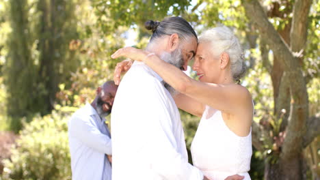 embracing at outdoor wedding, senior bride and groom smiling with friend standing in background