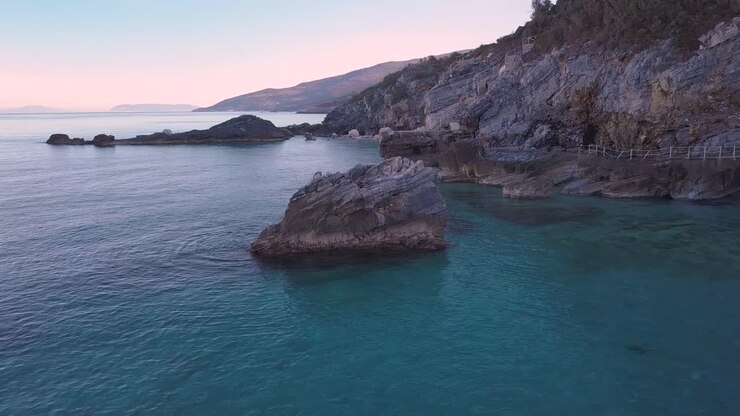 Ripresa aerea con drone in orbita antioraria di una grande roccia nelle acque cristalline del mare in Grecia