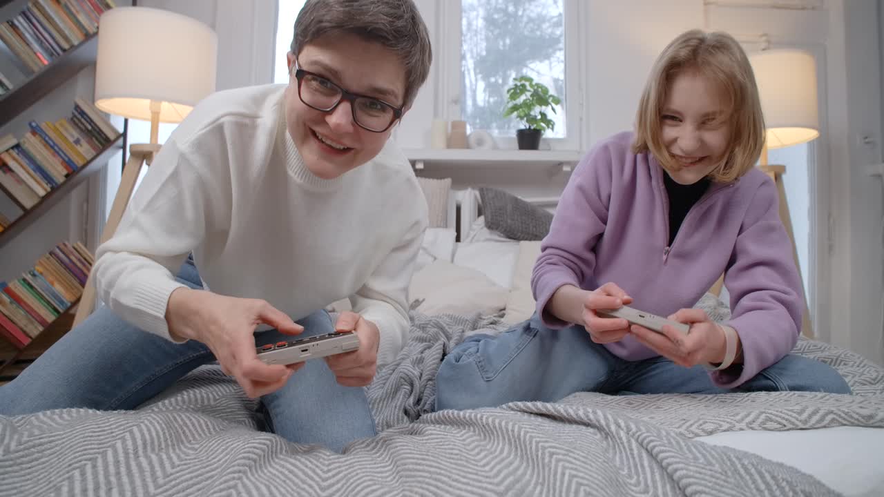 Mother and daughter playing handheld video games on a bed