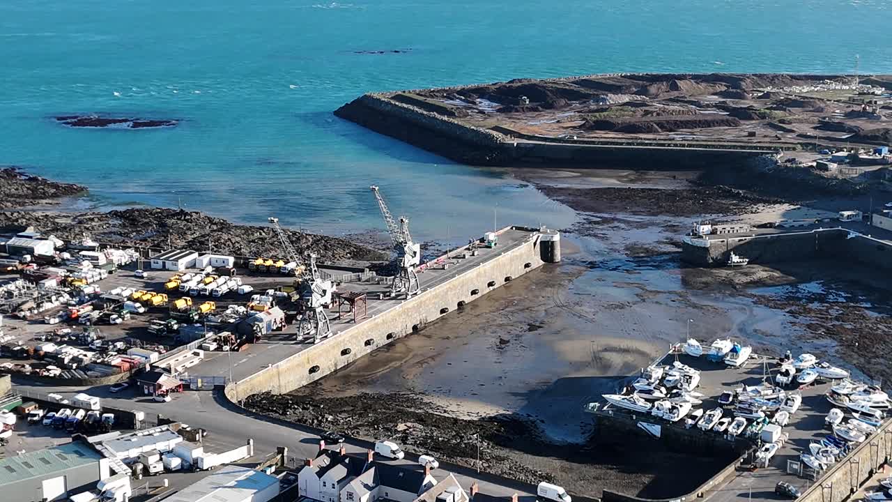 Guernsey St Sampsons.Dropping and circling drone footage of harbour entrance at low tide in late afternoon sun showing docks,boatyards,marina against background of clear water and blue sea