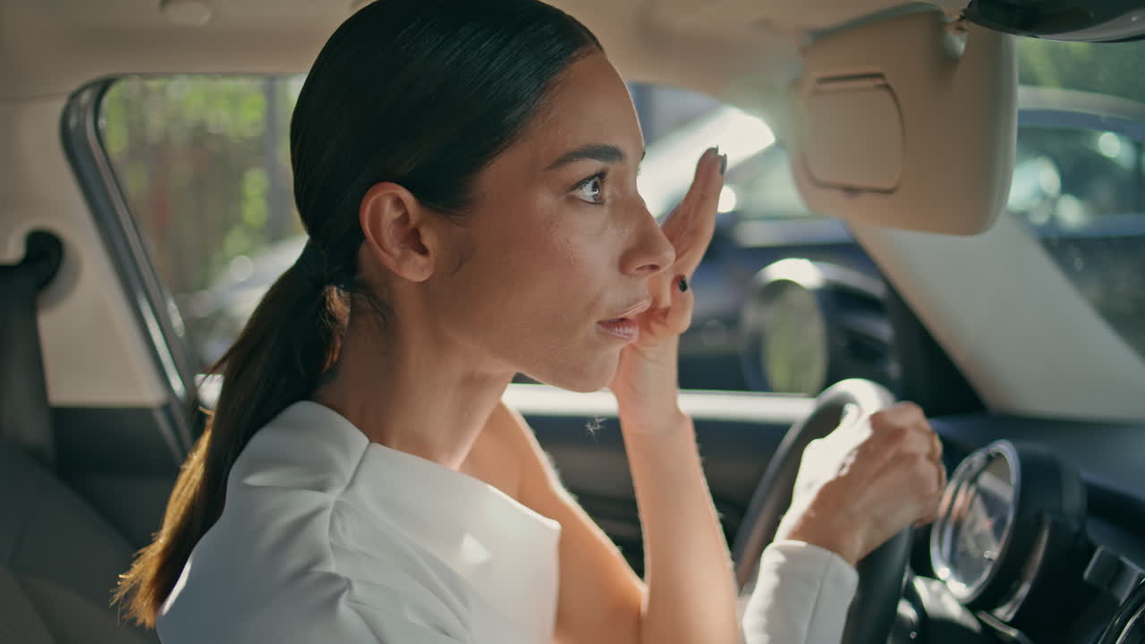 Brunette looking car mirror sitting front seat close up. Woman looking camera