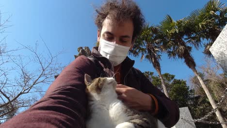 joven gato acariciador mientras usa mascarilla durante la crisis de la corona
