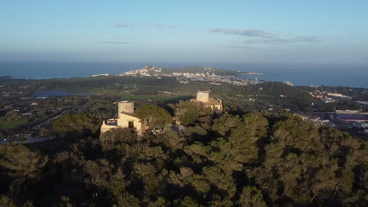 Aproximação aérea a casas no topo de uma colina com vistas para Cala Rajada ao pôr do sol, Maiorca, Espanha.