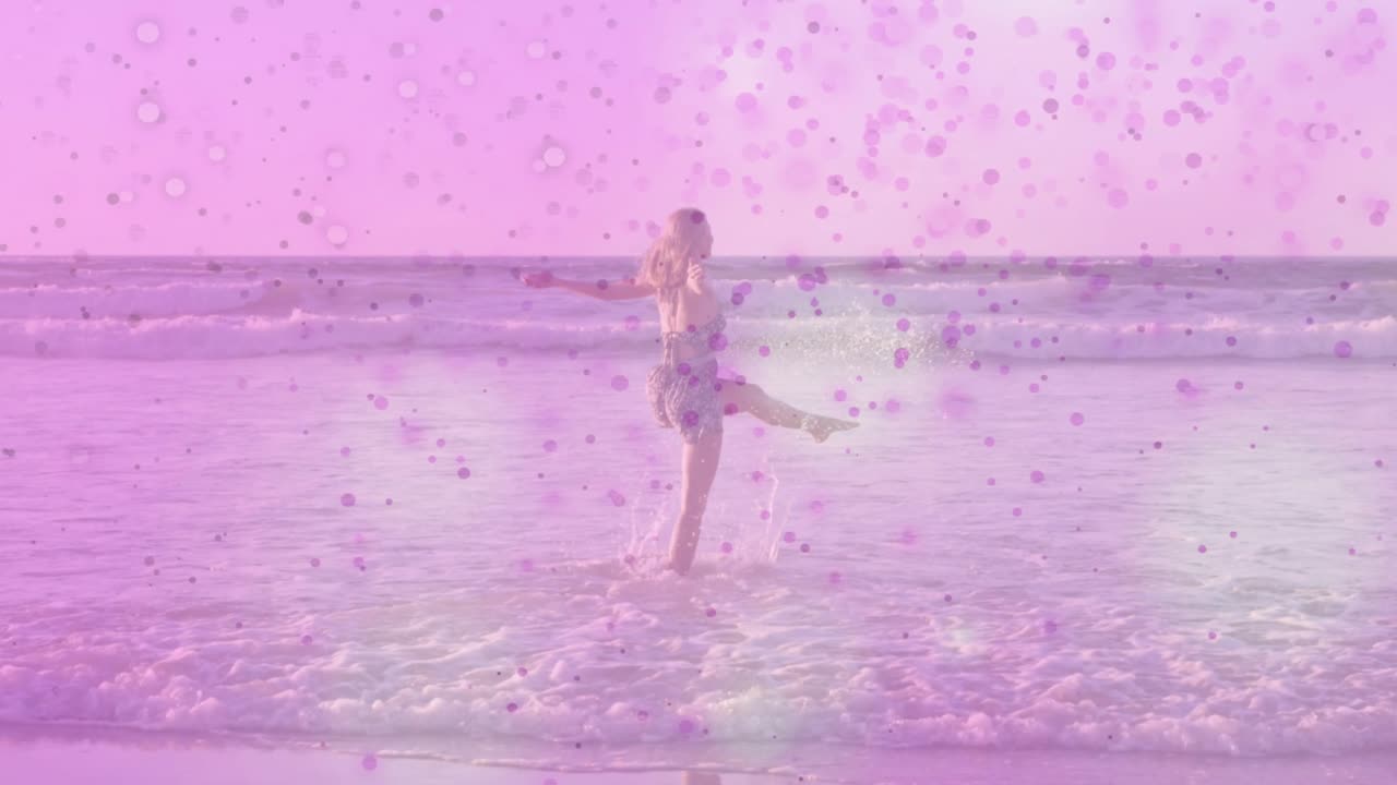 Donna che percepisce un'onda in arrivo e balla nella bassa risacca per il benessere con una sovrapposizione di coriandoli rosa