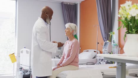 médico afroamericano con estetoscopio examinando a una paciente caucásica anciana en el hospital