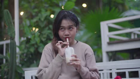 young woman enjoying a cold drink in an outdoor cafe surrounded by lush greenery
