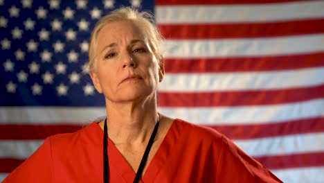 Medium-tight-portrait-of-nurse-looking-very-worried-and-sad-with-American-flag-behind-her
