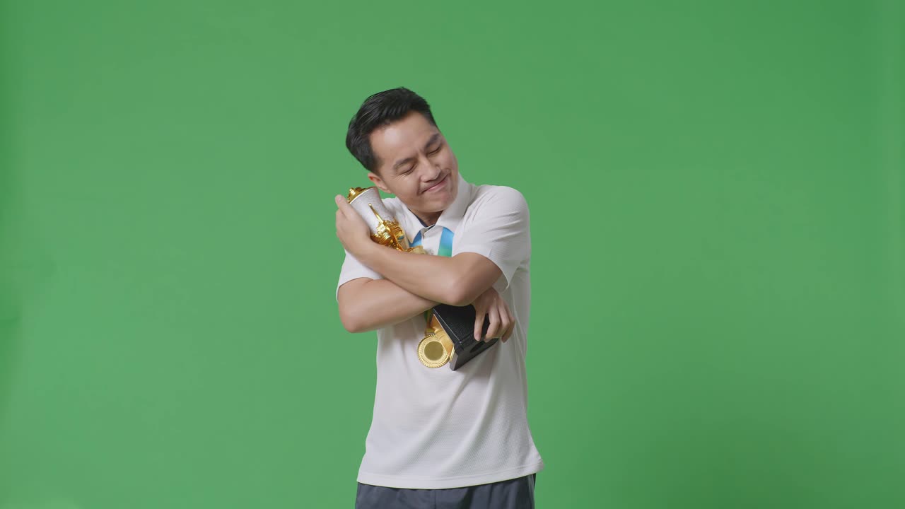 금메달을  아시아인, 금 트로피를 안고, 스튜디오의 녹색 스크린 배경에서 첫 번째 우승자로 자랑스럽게 승리합니다.