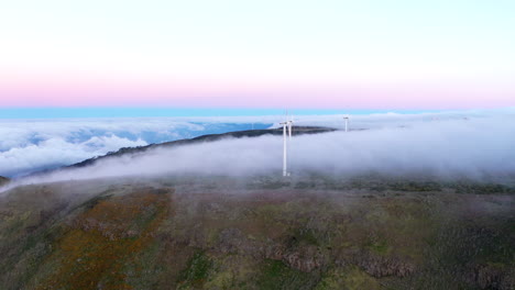 drone aerial footage flying over mountains with rolling clouds and wind turbines on the island of madeira, portugal