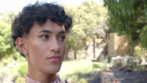 standing outdoors, non binary person with curly hair looking away thoughtfully