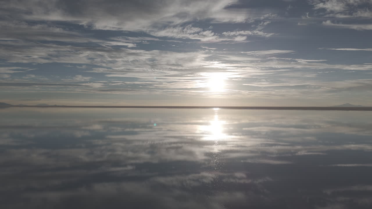 Drone shot flying over the salt flats in Uyuni Bolivia during sunset with reflection in the water going towards the sun LOG