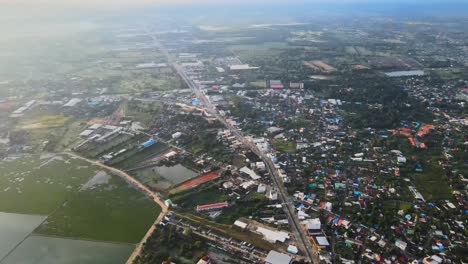 aerial: establishing shot: drone panning up high above the highway which separates the asian village, nakhon ratchasima town in korat province, thailand asia