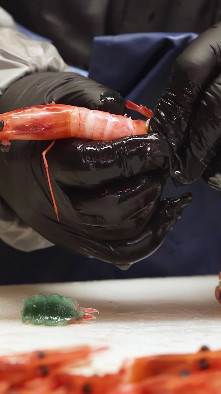 Close-up of hands peeling raw prawns in a professional kitchen in Tokyo, Japan.