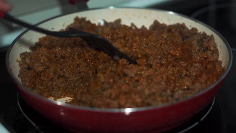 stirring ground beef and sauce in red pan