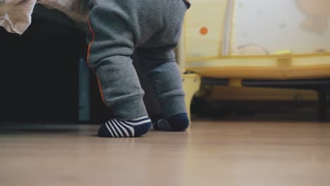 funny-baby-in-grey-pants-plays-at-bed-on-wooden-floor