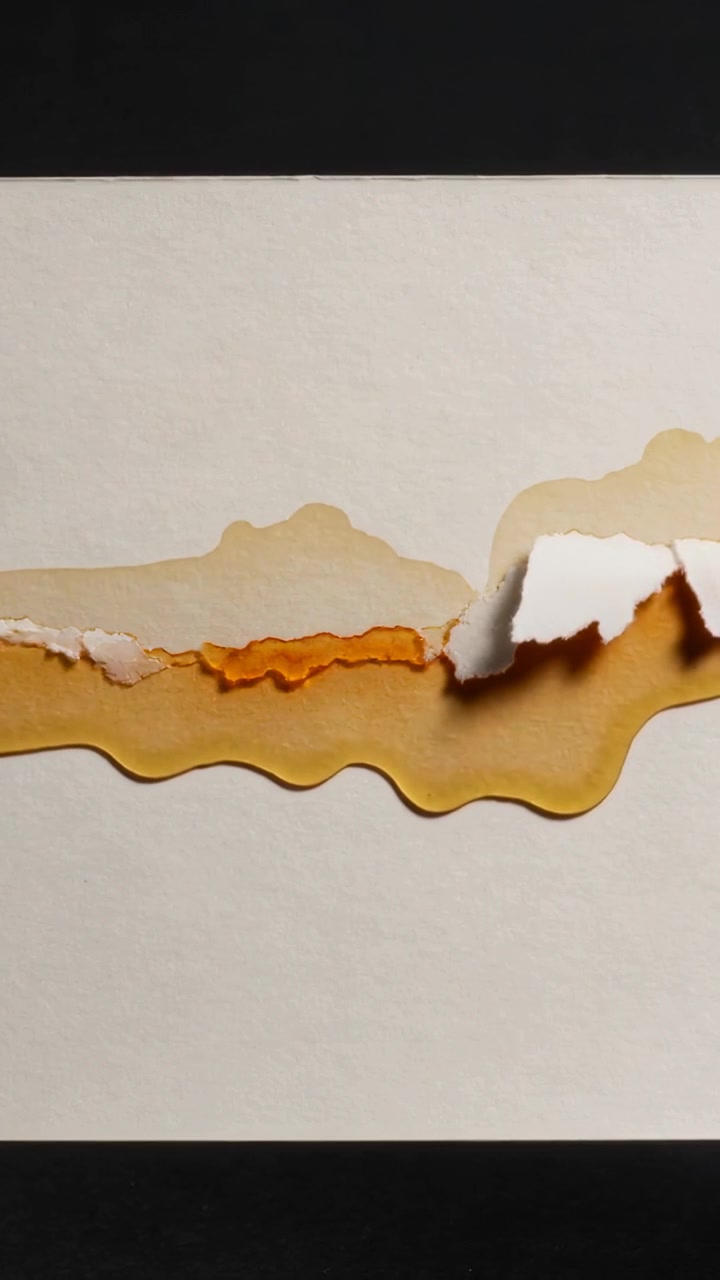 Vertical video: Lifting torn sheet flap right on dark mat, exposing orange layer and amber stain