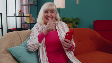la abuela mayor usa el teléfono móvil para comprar en línea, descubre una gran ganancia, celebra en casa.