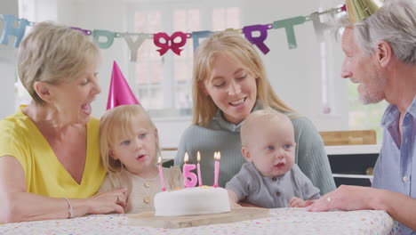 grandparents with mother at party singing happy birthday to granddaughter on fifth  birthday at home