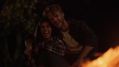 una pareja divertida riendo juntos en un campamento nocturno. los millennials sonrientes tienen citas románticas.