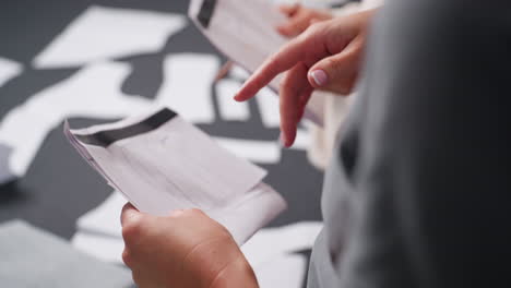closeup view of stylists demonstrating cloth designs drawn on white paper sheets during creative planning session, holding pattern sketches while fabric samples are visible in workspace indoors