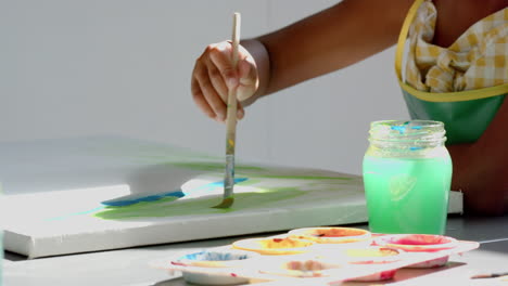 child painting on canvas with brush and watercolors in school art class