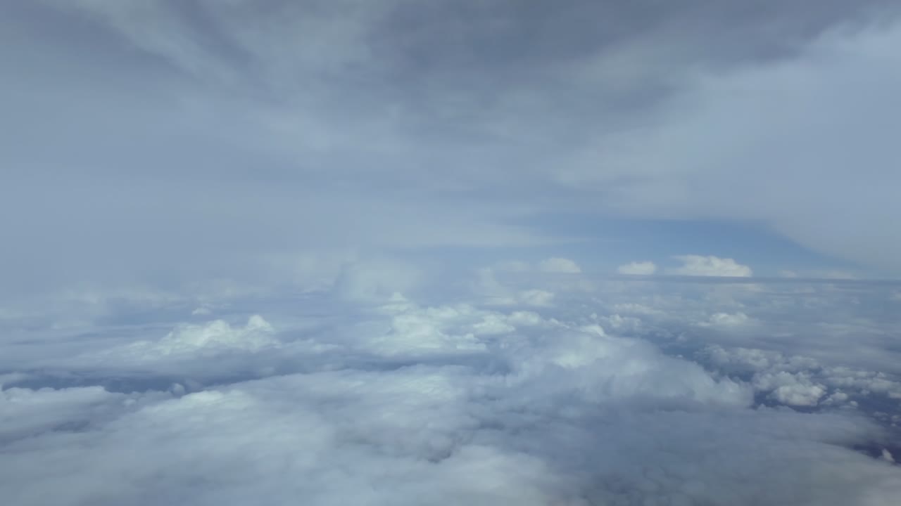 An immersive pilot’s view from a jet cockpit emerging from dark clouds into a clear blue sky with threatening storm cumulus clouds ahead. Footage taken at 10000m high from cockpit