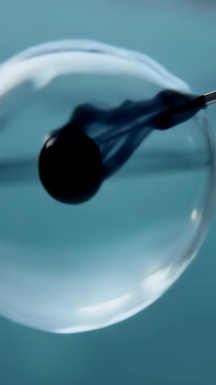 Video verticale: ago che tocca una bolla rilasciando filamenti di inchiostro in un macro studio, formando vortici scuri
